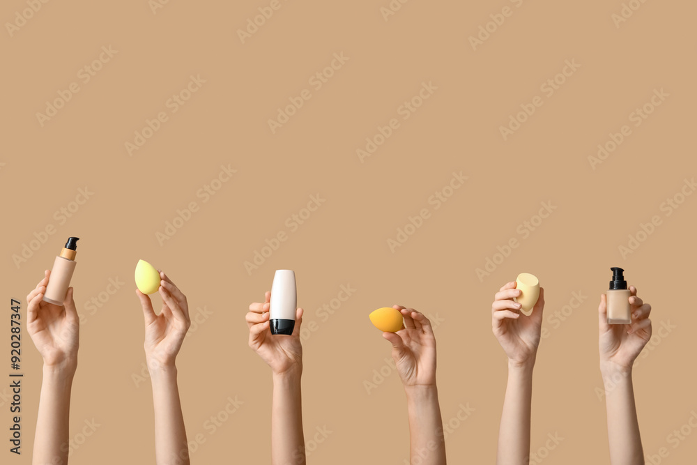 Wall mural female hands with makeup foundation and sponges on brown background