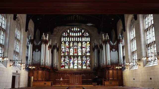Inside a cathedral or catholic church look at stained glass windows, pews, an organ, and pipes with beautiful sunlight shining through.