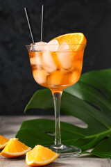 Glass of Aperol spritz cocktail and palm leaf on grey tile table