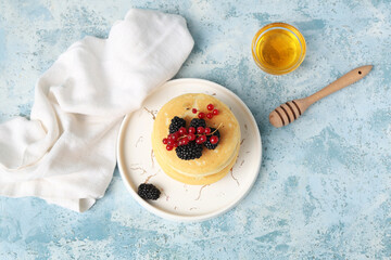 Plate of sweet pancakes with fresh blackberries, red currants and bowl of honey on light blue background