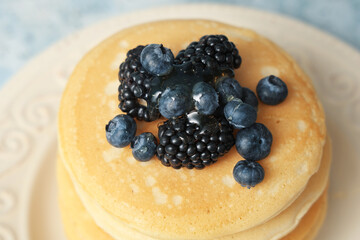 Plate of sweet pancakes with fresh blueberries and blackberries on light blue background, closeup