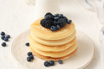 Plate of sweet pancakes with fresh blueberries and blackberries on white background