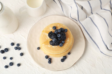 Plate of sweet pancakes with fresh blueberries, blackberries and jug of milk on white background