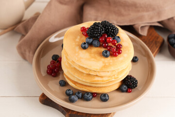 Plate of sweet pancakes with different fresh berries on white wooden background