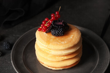 Plate of sweet pancakes with fresh blackberries and red currants on black background