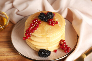 Plate of sweet pancakes with fresh blackberries and red currants on wooden background