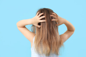 Little girl with pediculosis scratching her head on blue background, back view