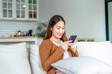 Happy young asian woman relax on comfortable couch at home texting messaging on smartphone, smiling girl use cellphone chatting