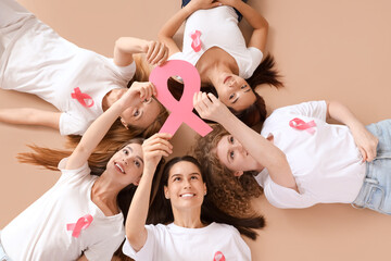 Beautiful women with pink ribbons lying on beige background, top view. Breast cancer awareness...