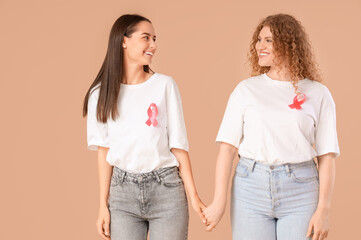Beautiful women with pink ribbons holding hands on beige background. Breast cancer awareness concept