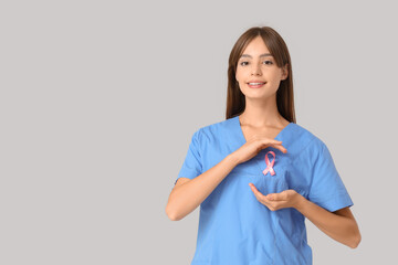 Female doctor with pink ribbon on light background. Breast cancer awareness concept