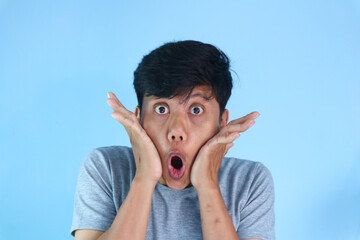 Shocked face of Asian young man in grey t-shirt on a isolated background.