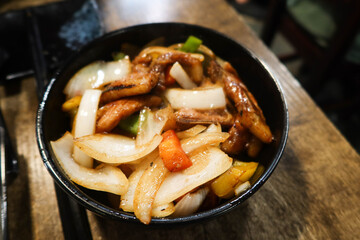 close up of Chinese style stir fried pork chop with onion, pepper in a black bowl