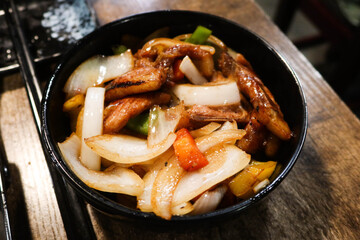 close up of Chinese style stir fried pork chop with onion, pepper in a black bowl