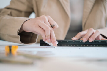 The Asian woman, a skilled architect and designer, meticulously draws up the blueprint using a...