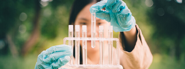 The woman conducted outdoor biology research, using a test tube in the field to perform chemical analysis, demonstrating the practical application of science. © Atthapon