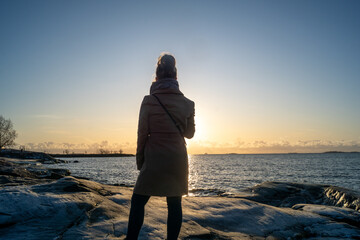 lonely blond woman on the beach in Helsinki Finland on a cold winter day watching sunset