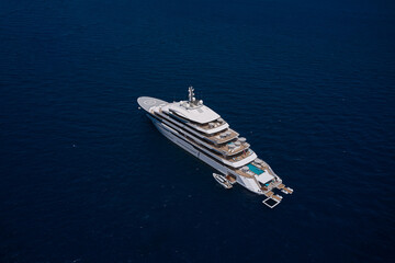 Luxury big white mega yacht with helipad top view in open sea. Expensive white charter yacht against the background of dark blue sea, aerial view.