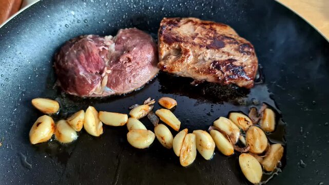Pork loin joint steak fry in oil pan, side of roasted garlic cloves, cooking