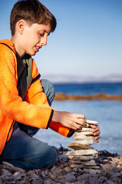 Cute boy stacked pebble stones tower on the beach
