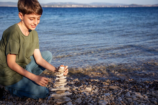 Cute boy stacked pebble stones tower on the beach