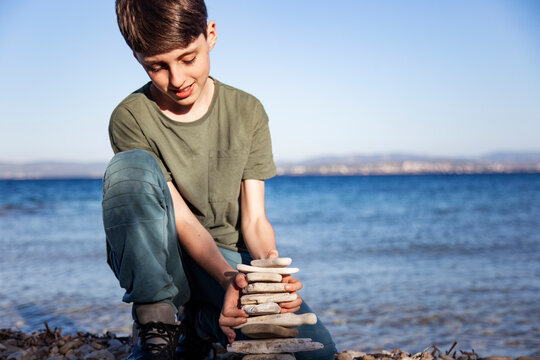 Cute boy stacked pebble stones tower on the beach