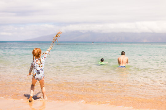 Little girl throwing sand at her brothers as they swim away