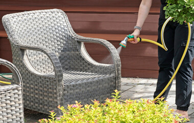 Anonymous cleaning, hose water washing wicker furniture from summer. Structures in backyard....
