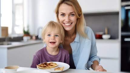 Portrait of the mother and her child in the kitchen, smiling while holding crepes on a white plate with a chocolate spread. 