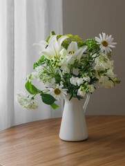 A bouquet of summer flowers in a metal jug on a round wooden table in the living room
