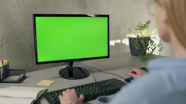 Young Woman Working In Office On Desktop Computer with Green Screen Mock Up Display. Over the Shoulder- Close-up of Monitor With Green Screen Chromakey