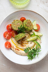 Hummus served with paprika, falafel, fresh tomatoes and cucumber in a beige plate, middle close-up, vertical shot, high angle view