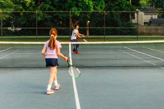 Father and child play tennis together on tennis court in summer