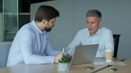 Two men in an office discussing business while one writes on a notepad.