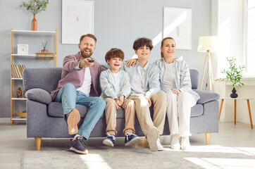 Obraz premium Happy family, parents and children enjoying leisure time together at home. Sitting on the sofa, watching TV or a movie. Family bonding and shared activities in the comfort of home.