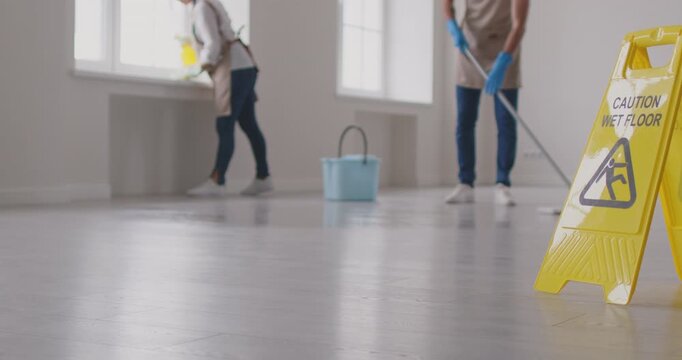 Cleaner group working, floor washing, yellow wet caution sign, professional janitor service busy completing cleaning tasks at home, office. Taking care of room, maintaining hygienic sanitary mopping