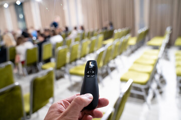 A hand firmly grasps a clicker in a conference room that is filled with numerous empty chairs...
