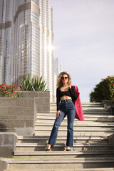 girl with jacket standing on stairs on street against background of high-rise building