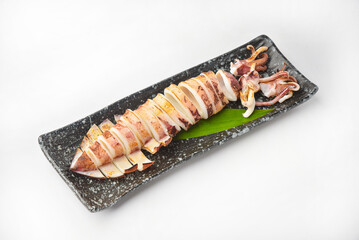 A long grilled squid sits on a black plate ready to eat.