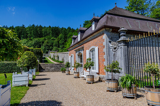 Renaissance style building next to gravel path in Freyr Castle garden, wooden flower pots, mountain with trees in background against blue sky, sunny summer day in Namur, Wallonia, Belgium