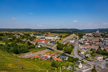 Obraz premium Aerial view of Givet city outskirts, bridge crossing railway tracks, vehicular streets, buildings, houses, trees in field and horizon in background, sunny summer day in Ardennes department, France