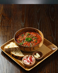 Traditional Ukrainian food is borscht, in a wooden bowl, with a piece of meat, bread and garlic, garnished with herbs.