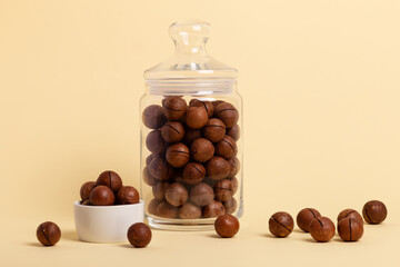 Shelled macadamia nuts in a glass container and in small white plate on a beige background. Tasty and healthy macadamia nuts. Healthy snack. 