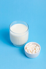 Many lactase tablets in small white plate and a glass of milk containing lactose on a blue background. lactase tablets for assimilation of lactose from dairy products. Lactose intolerance.