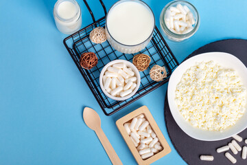 Lactase tablets, yogurt containing lactose, milk, cottage cheese and a wooden spoon from above on a blue background. Lactase enzyme for assimilation of lactose from dairy products. Rustic style
