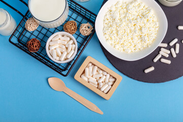 Lactase tablets, yogurt containing lactose, milk, cottage cheese and a wooden spoon from above on a blue background. Lactase enzyme for assimilation of lactose from dairy products. Rustic style