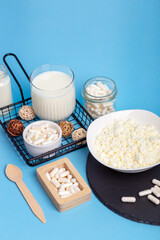 Lactase tablets, yogurt containing lactose, milk, cottage cheese and a wooden spoon on a blue background. Lactase enzyme for assimilation of lactose from dairy products. Rustic style