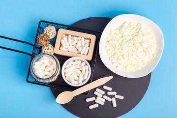 Many lactase tablets, cottage cheese and a wooden spoon on a black round stone desk on a blue background from above. Lactase enzyme for assimilation of lactose from dairy products. Rustic style. Top.
