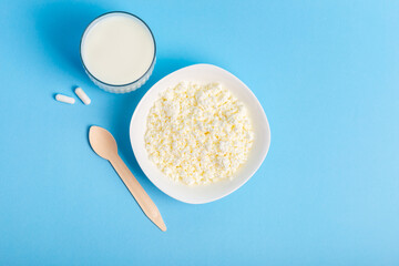 Lactase tablets, milk and cottage cheese containing lactose and a wooden spoon from above on a blue background. lactase tablets for assimilation of lactose from dairy products. Lactose intolerance. 