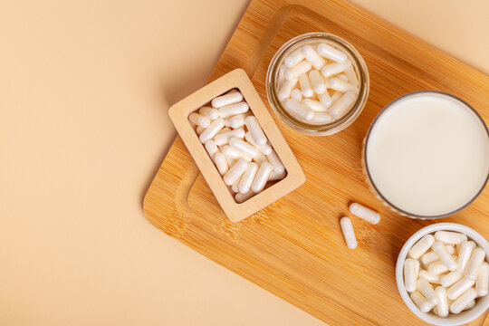 Lactase enzyme tablets in a wooden box and in a ceramic white plate, in a glass jar, a glass of milk on wooden desk on beige background top view. Lactose intolerance. Dairy products containing lactose